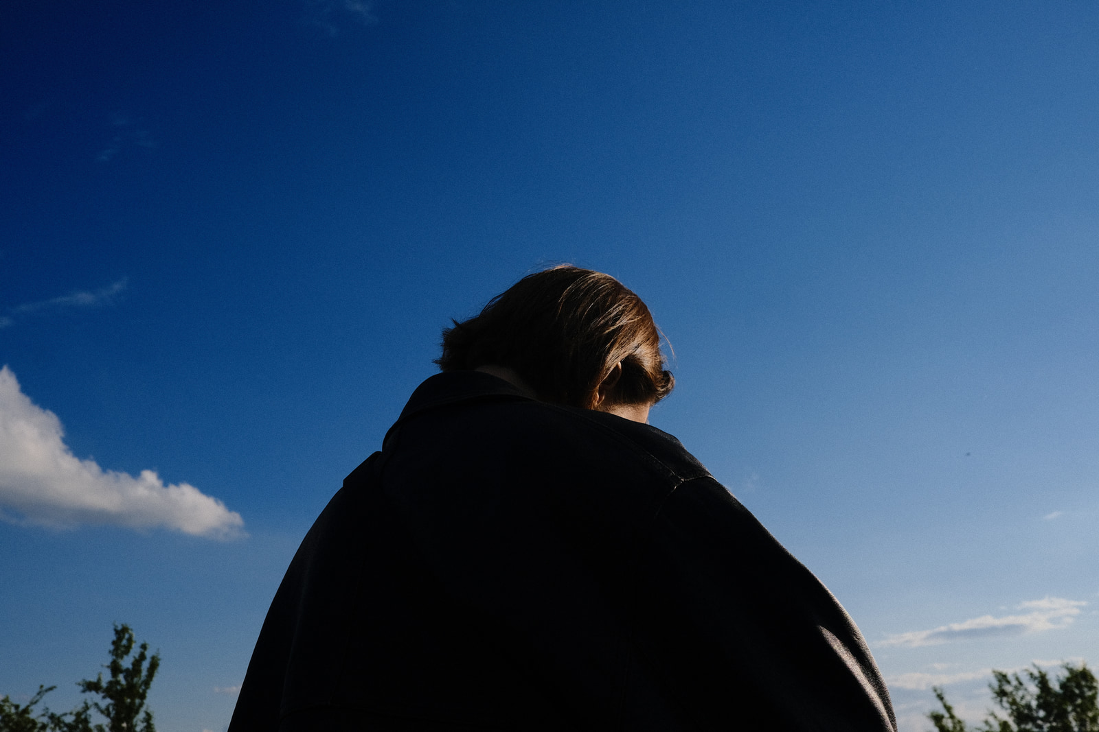 A person stands with their back to the camera, gazing out over a clear blue sky with a few wispy clouds.