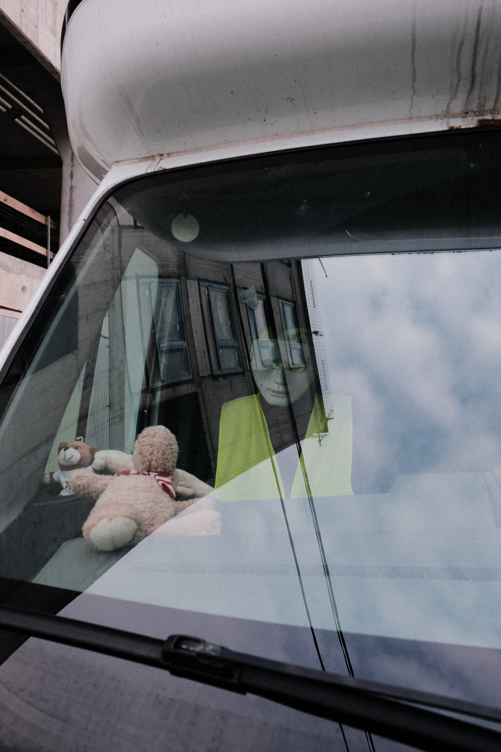 A teddy bear rests on the dashboard of a car, viewed through the windshield.