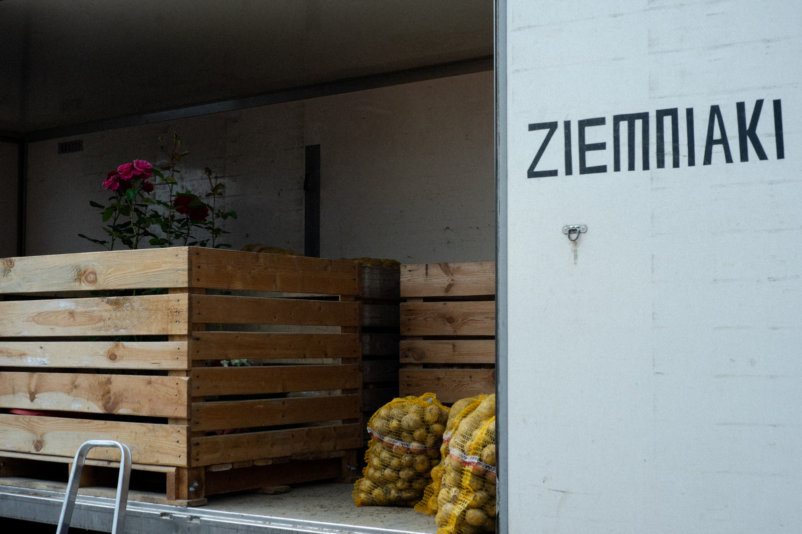 Wooden crates and sacks of produce are stacked near an open doorway, with a potted plant visible on the crates.