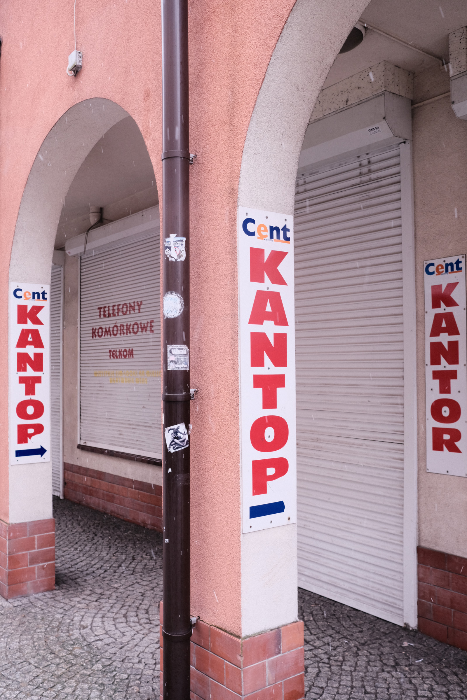 Closed storefronts with metal shutters and signage for "Cent Kantor" on a pink building.