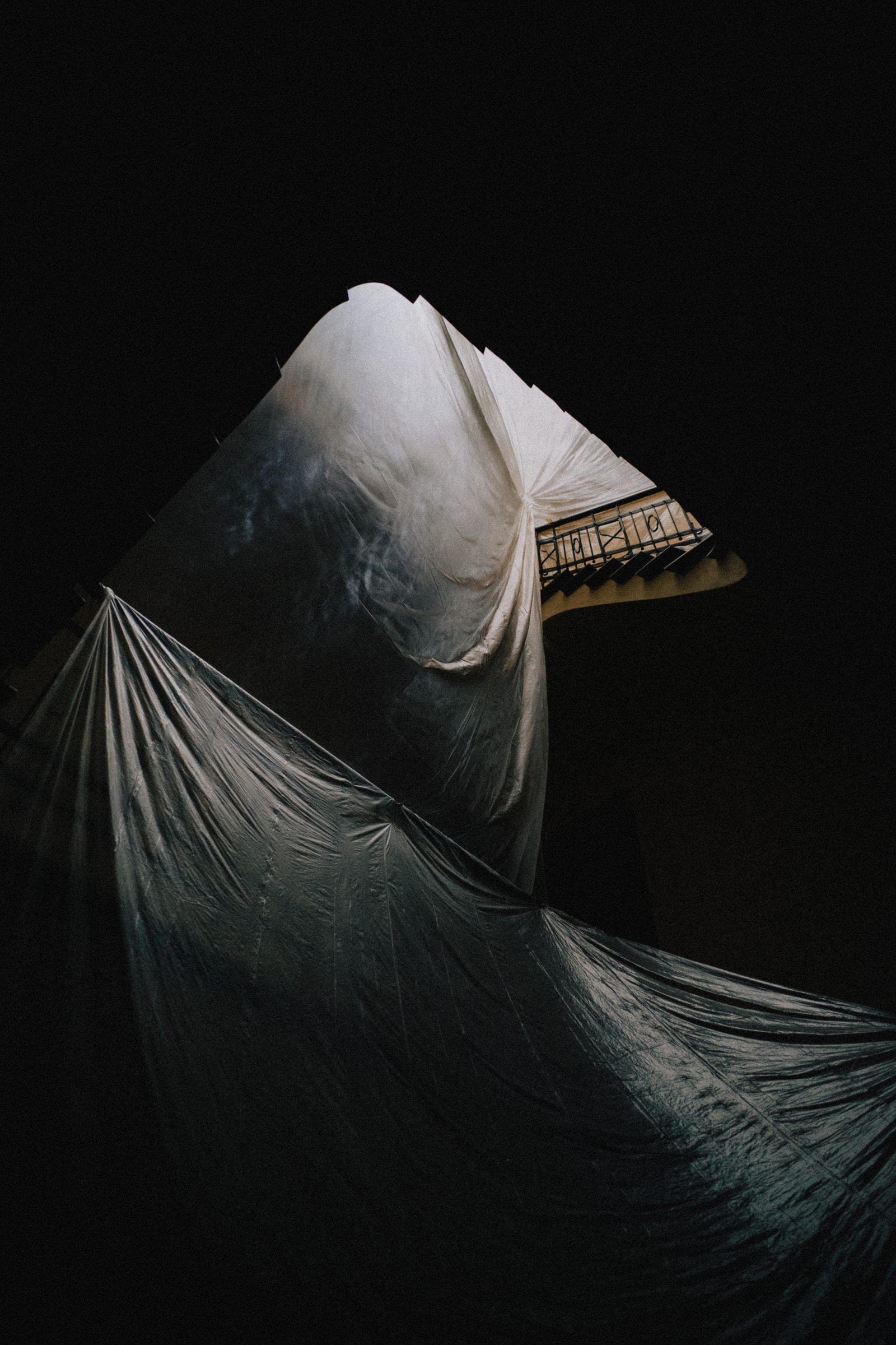 A large, draped white fabric partially covers a structure, with a dark background emphasizing the shape and texture of the material.