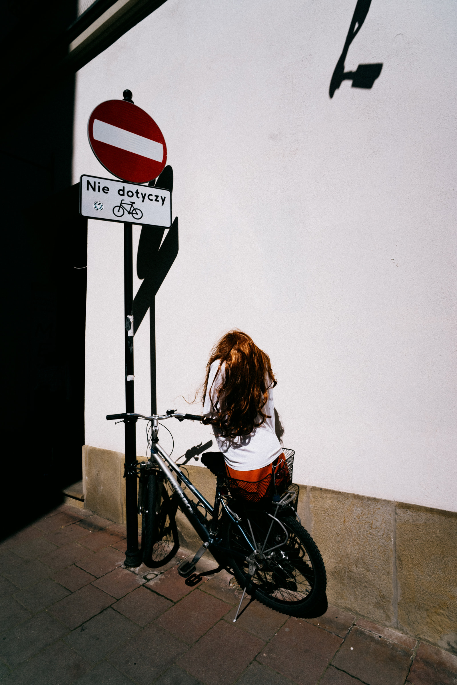 A person sits on a bicycle leaning against a signpost near a building.