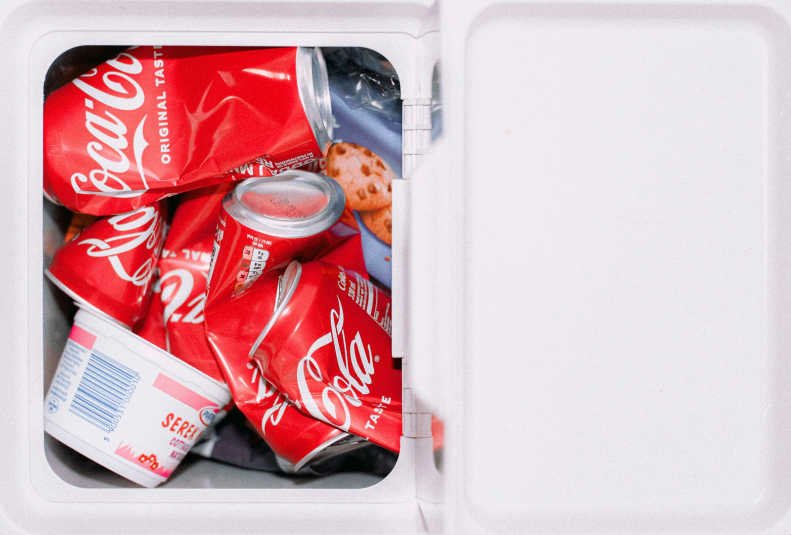 Opened cooler containing several cans of Coca-Cola and a package of cookies.
